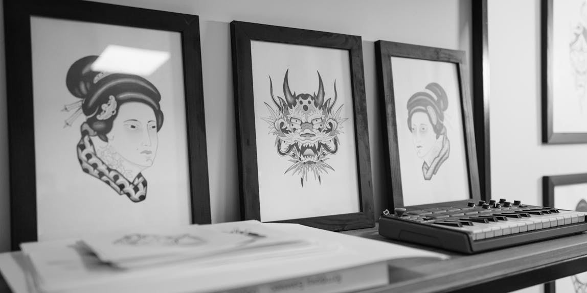 Monochrome art prints and compact synthesizer placed on a sleek shelf in an indoor setting.