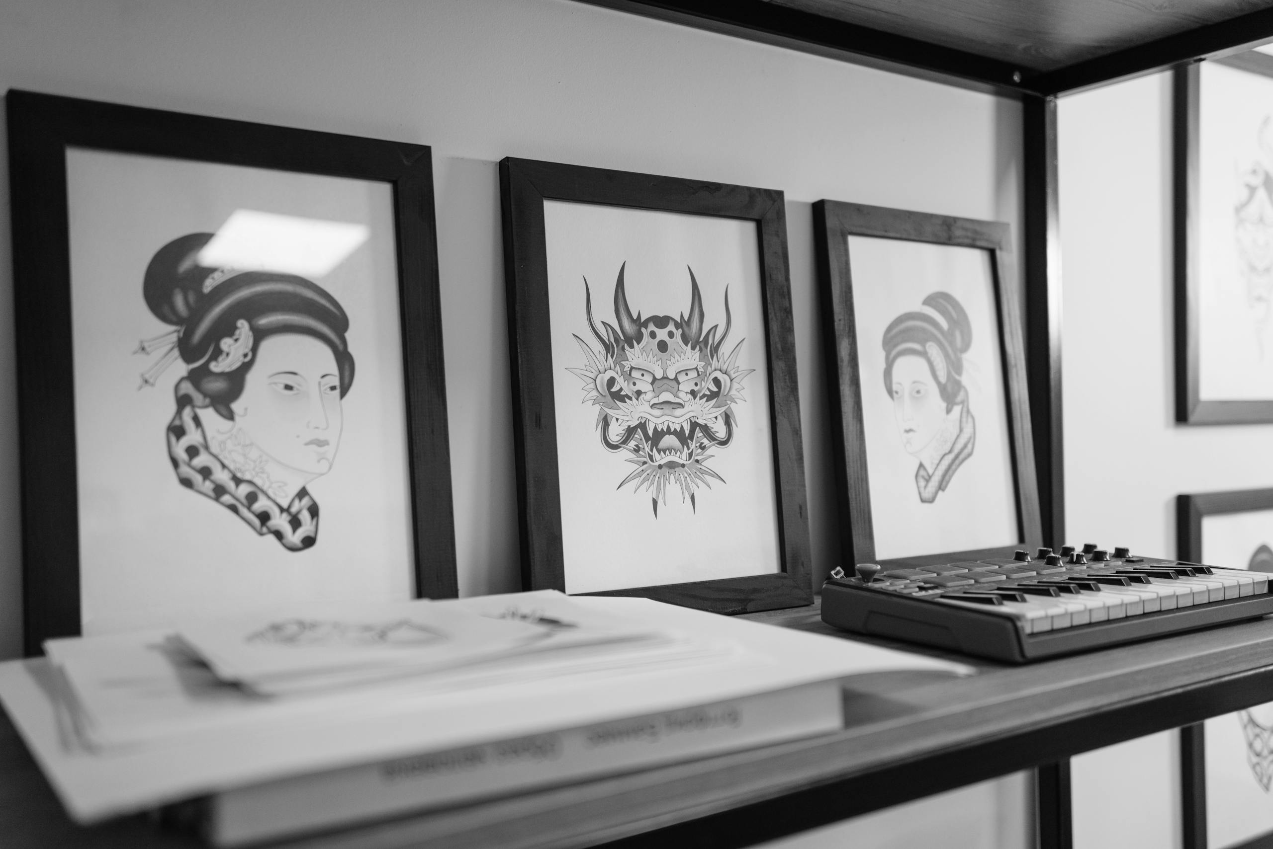 Monochrome art prints and compact synthesizer placed on a sleek shelf in an indoor setting.